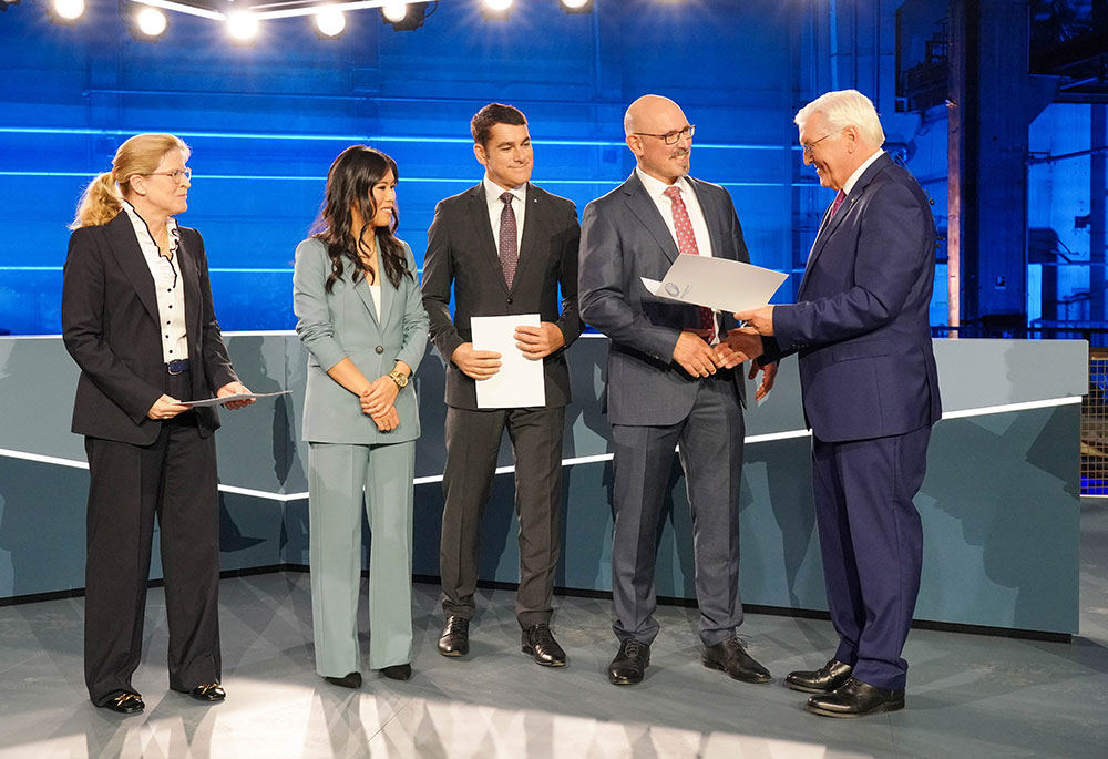 Bundespräsident Frank-Walter Steinmeier, Moderatorin Mai Thi Nguyen-Kim und das Team der Brainlab AG stehen auf der Bühne bei der Verleihung des Deutschen Zukunftspreises 2022, Foto: Deutscher Zukunftspreis