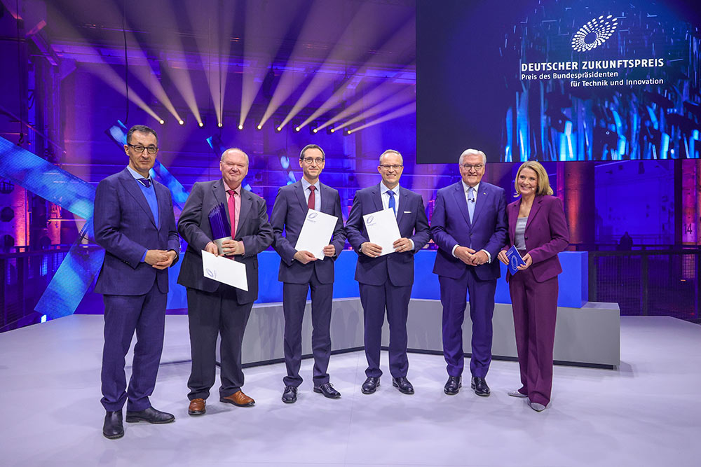 Cem Özdemir, Dr.-Ing. Hermann Oppermann, Dr. rer. nat. Norwin von Malm, Stefan Grötsch, Bundespräsident Frank-Walter Steinmeier und Moderatorin Yve Fehring stehen auf der Bühne bei der Verleihung des Deutschen Zukunftspreises 2024, Foto: Deutscher Zukunftspreis Bildschön