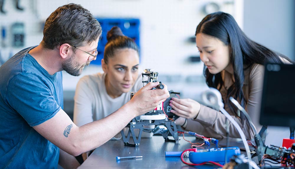 Ein junger Mann und zwei junge Frauen bauen an einem technischen Modell, Bild: iStock.com, FatCamera