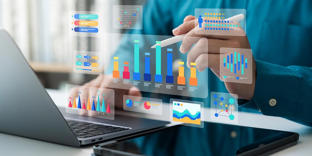 Peron arbeitet an einem Laptop und einem Tablet, Diagramme schweben im Raum dazwischen, Bild. iStock/ThapanaOnphalai