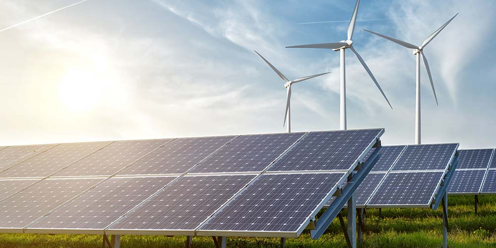 Solarpanele auf einem Feld, Windräder im Hintergrund, Bild: iStock/artJazz