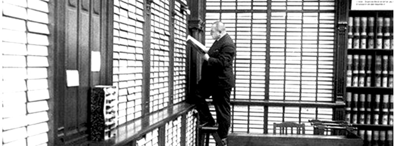 Alt-Text: Seinerzeit in der Bibliothek: Mann steht auf Leiter vor Regalreihen