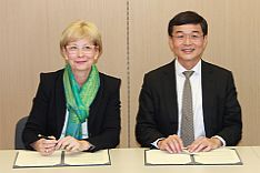 Deutsche Amtschefin und Kollege aus Singapur sitzen am Tisch und unterschreiben Vertrag
