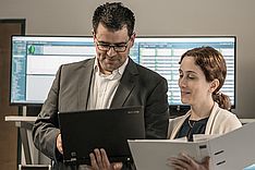 Zwei Personen mit Aktenordnern vor IT-Landschaft