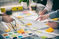 A desk with hands, papers, colour samples and mugs