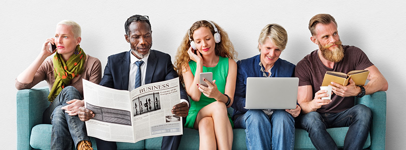 Five men and women sitting on a sofa using different media like phone, notebokk, newspaper etc